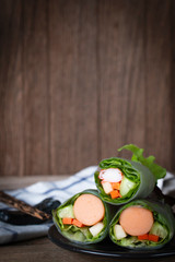 Salad rolls on black plate placed on a wooden table with chopsticks and White Blue Striped Fabric placed backside.