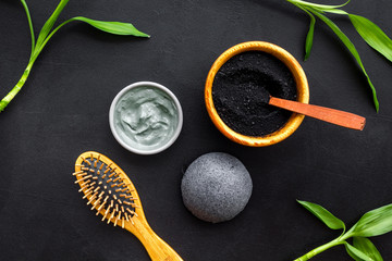 Hair care, hair spa. Cosmetics based on bamboo charcoal powder near comb on black background top...