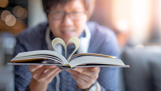 Asian happy man holding book with heart shape page folded in the center. Reading for World book day. Love and valentine concepts