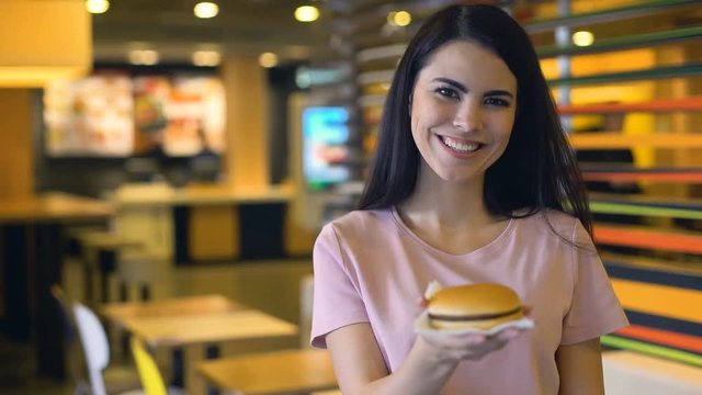Happy woman enjoying smell of tasty burger and smiling on camera, sandwich club