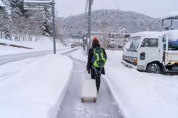 traveler with backpack and luggage walking on snow covered road in winter at Takayama Japan