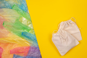 Many multicolored plastic bags with one eco natural reusable bag for shopping on yellow background. Zero waste, eco friendly, sustainability lifestyle, no plastic concept