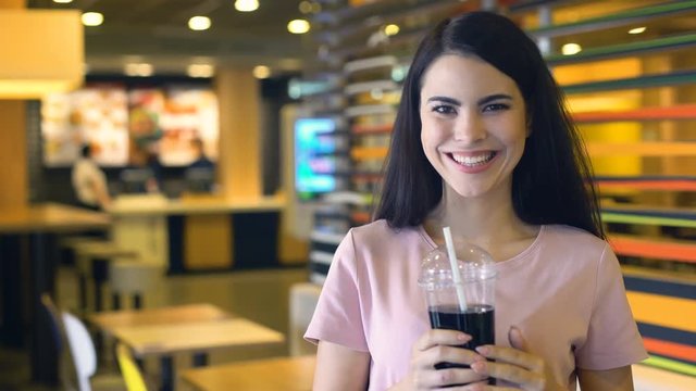 Attractive young woman drinking juice from plastic cup and smiling, soft drink