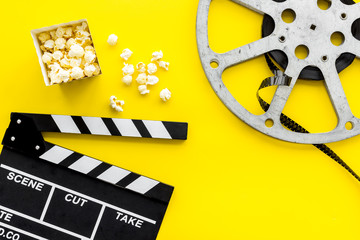 Movie premiere concept. Clapperboard, film stock, popcorn on yellow background top view copy space
