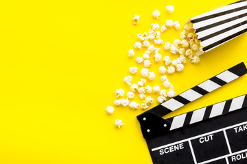 Naklejka premium Movie premiere concept. Clapperboard and popcorn on yellow background top view space for text