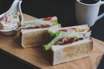 Appetizing sandwich on a wooden board with filling from lettuce, slices of fried bacon and tomato