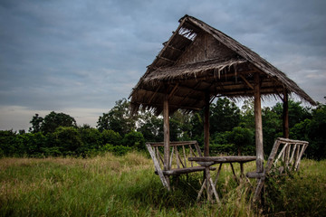 Wooden arbor with a roof made of rice straw. Resting place in a field next to a small forest. Shadow in clear weather in Thailand. Photos of benches from logs.