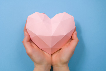 Hands holding a paper polygonal pink heart