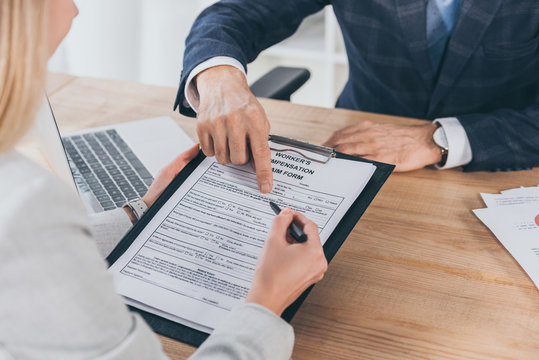 cropped view of businessman in blue jacket pointing on form for compensation claim with finger to woman in office, compensation concept