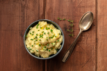 Pomme puree, an overhead photo of a bowl of mashed potatoes with herbs, shot from the top on a rustic background with a sprig of thyme and copy space