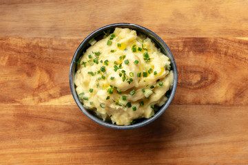 Pomme puree, an overhead photo of a bowl of mashed potatoes with herbs, shot from the top on a rustic background with a place for text
