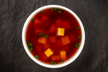 Miso shiru soup with tofu and scallions, shot from above on a black background