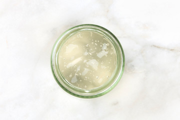 A glass jar with aloe vera gel, shot from above on a white marble background with copy space