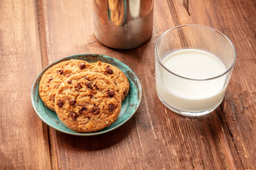 A closeup photo of chocolate chip cookies with milk on a dark rustic wooden background with copy space