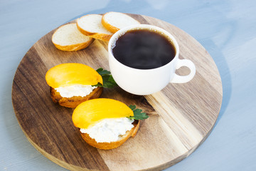 Bruschetta with fresh cottage cheese and persimmon and hot coffee. Traditional homemade breakfast. Close-up. Place for text. Top view.