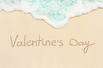 Fototapeta na wymiar Happy valentine's day handwritten on the sand beach with blue ocean wave on background