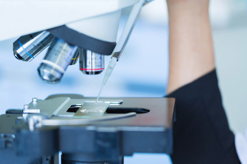 Scientist dropping chemical liquid on the slide at microscope, concept science and technology