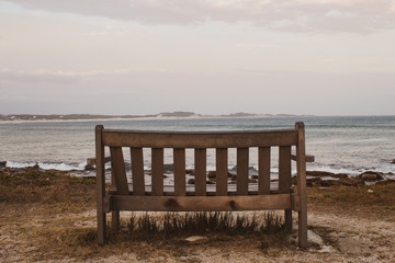 Fototapeta na wymiar A lonely wooden bench overlooking the south african wavy ocean; peace of mind concept