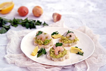 Small snack sandwiches on white bread with guacamole and shrimps on a white plate. Selective focus.