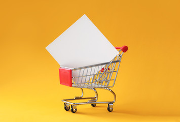 Creative shopping background with shopping cart and empty card in it on yellow background with copy...