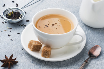 Cup of tea with milk, brown anise sugar on a grey table.