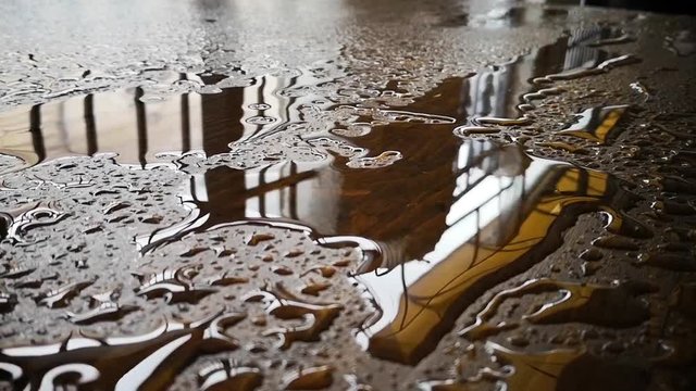 Color footage of a puddle of water and rain drops on a wooden platform.
