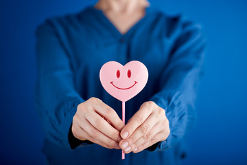 Woman hand giving pink heart shaped lollipop with smile on blue background