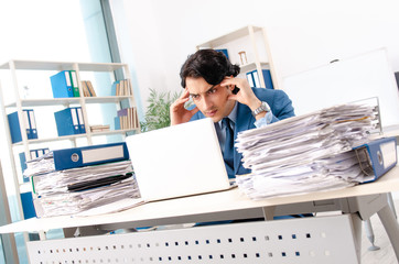 Young handsome male employee with too much work in the office