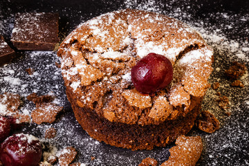 Round chocolate cake with cherry on a dark background. Everything is sprinkled with scoop sugar.