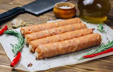 Raw Tyrolean sausages with rosemary over wooden background