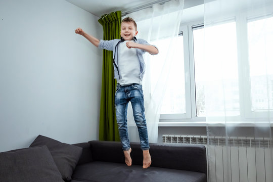 The boy jumps on the couch in the living room, having fun, fooling around, while his parents are not at home. Baby sitting, baby alone at home.