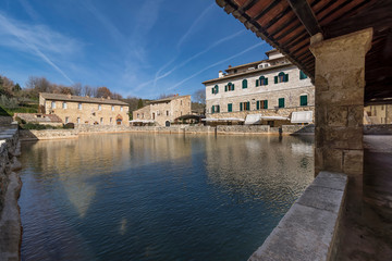 Beautiful view of the medieval village of Bagno Vignoni with its thermal bath and a sky crossed by aircraft trails, Tuscany, Italy