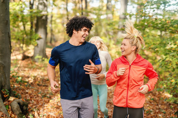 Sporty smiling friends running in forest at autumn. Fitness outdoor concept.