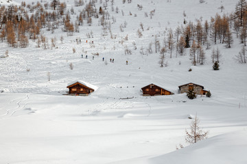 panoramic view of a mountain pasture with huts submerged by the snow on a sunny winter day.