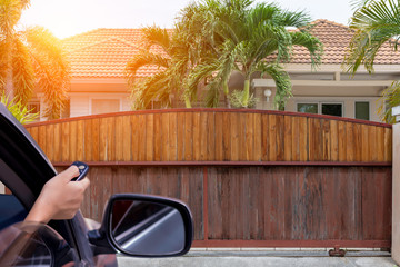 Woman in car, hand using remote control to open the wooden automatic gate with modern home...