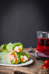 Salad rolls on white plate placed on a sack there is tomato and red water in glass placed beside.