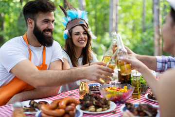 Group of happy friends eating and drinking beers at barbecue dinner