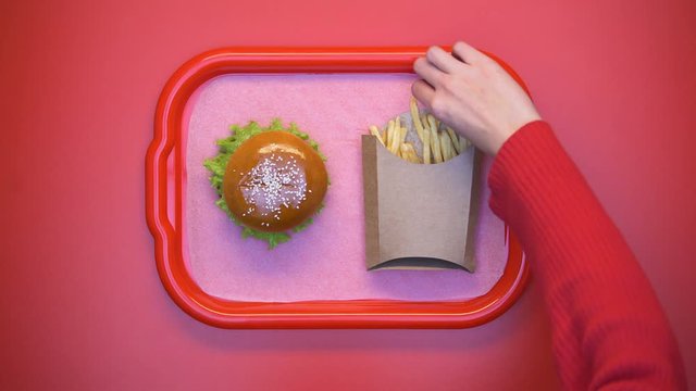 Female hand taking crunchy french fries from carton box on tray, fatty snack