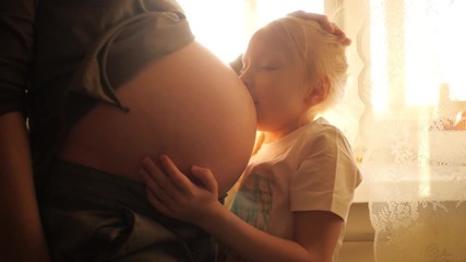 Happy 6 year old daughter kissing mom's pregnant belly. Slow motion, 4K UHD.
