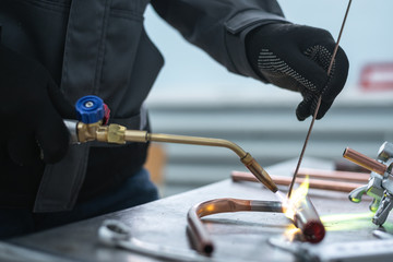 Worker is soldering a pipe by a blow lamp on a factory workbench background. Pipework.