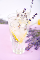 Lavender lemonade with lemon and ice on purple background.