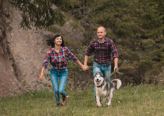 Naklejka na ściany i meble Male female with husky dog having fun on summer vacation. Portrait of a happy couple laughing. Summer holidays, love, relationship concept - smiling couple in mountains. Couple outdoors