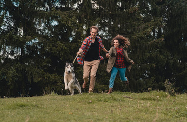 Naklejka na ściany i meble Man and woman walking with husky dog in the mountains. Young couple in love in mountains at sunset. Portrait of a happy couple smile to camera. Lifestyle concept. Banner