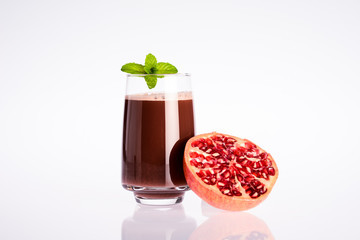 glass of pomegranate juice with open pomegranate and mint leaf on white background
