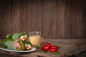 Salad rolls on white plate placed on a sack there is tomato and chilli placed beside and salad dressing placed backside.