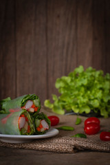 Salad rolls on white plate placed on a sack there is tomato and chilli placed beside and lettuce placed backside.