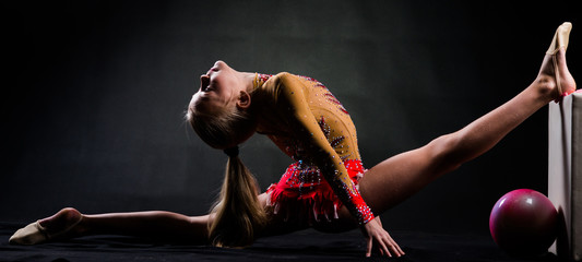 Beautiful teen girl doing rhythmic gymnastics exercises. Black background