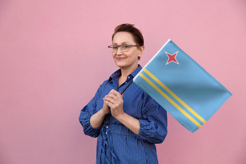 Aruba flag. Woman holding Aruba flag. Nice portrait of middle aged lady 40 50 years old holding a large flag over pink wall background on the street outdoor.