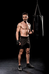 Fototapeta na wymiar handsome boxer standing near boxer bag on black background