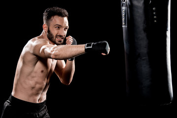 handsome bearded man exercising with punching bag isolated on black